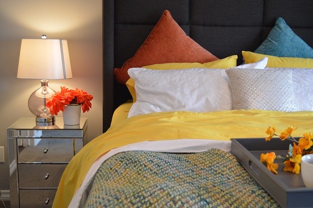 postel s barevnými polštáři a lampa na nočním stolku